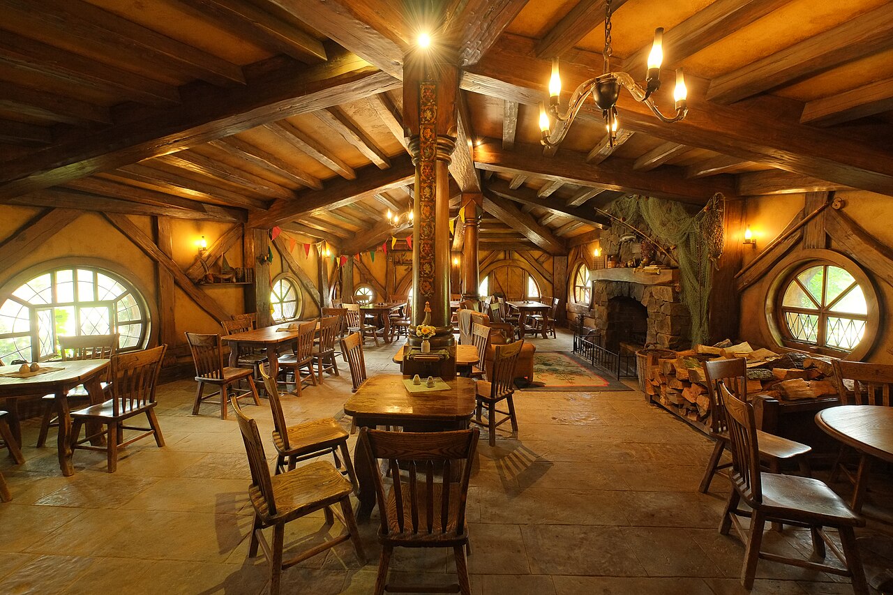 interieur green dragon inn pub hobbiton nouvelle zelande Intérieur du Green Dragon Inn avec ses tables en bois, ses chaises et ses fenêtres rondes