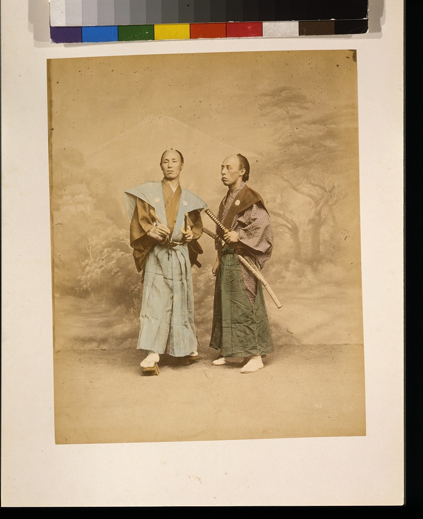 Deux hommes japonais possiblement samouraïs vers 1877 Deux hommes japonais portant chacun deux sabres dans un studio vers 1877